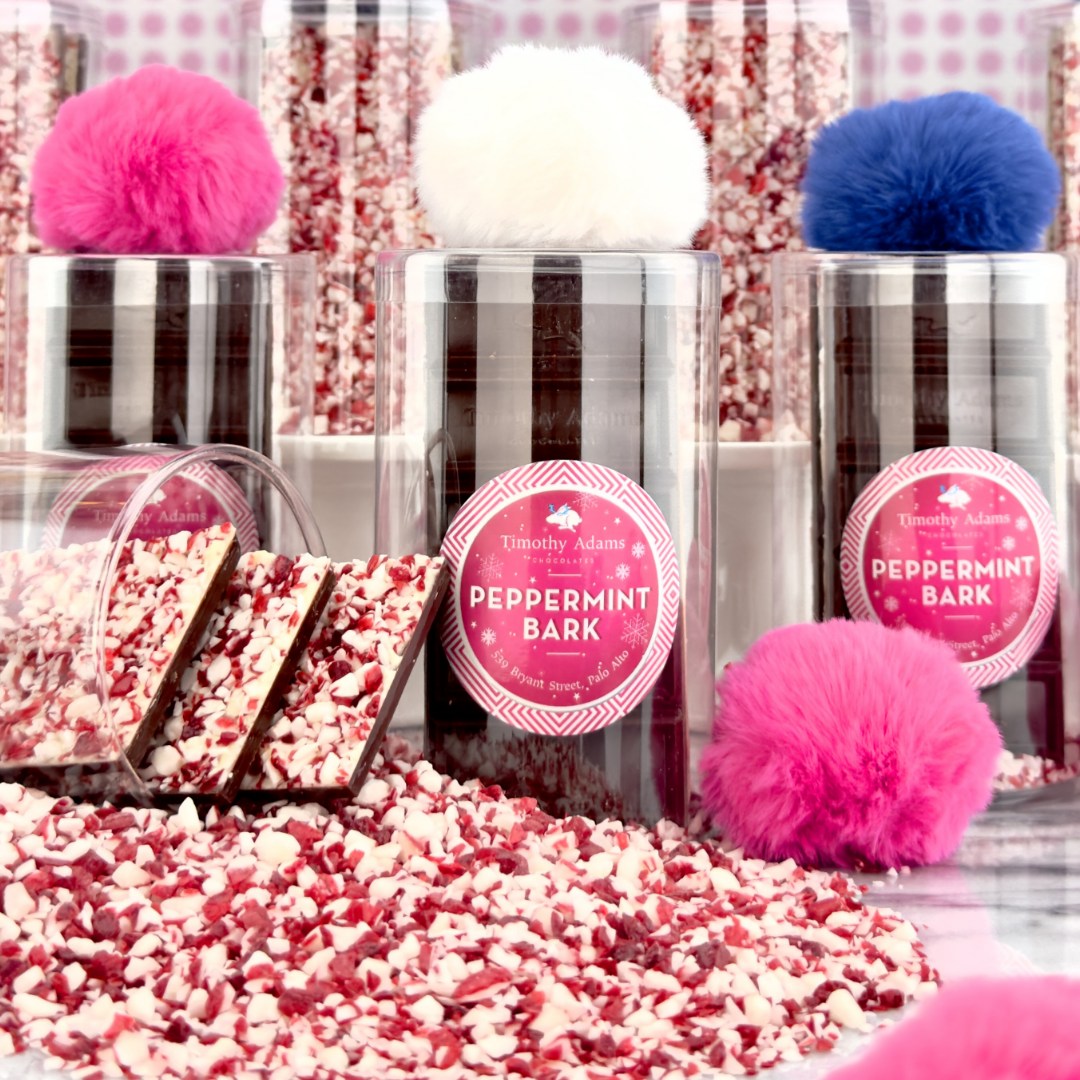 Clear tubes filled with peppermint bark pieces topped with bright pink, blue, and white pom-poms, surrounded by loose peppermint bark.