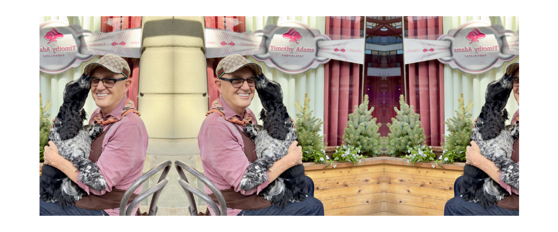 Tim the owner sits outside the shop, smiling as the black-and-white dog — Rosie, climbs into their lap to nuzzle them affectionately. Behind them is the storefront with a sign for the chocolate shop and a planter of small evergreens and flowers.